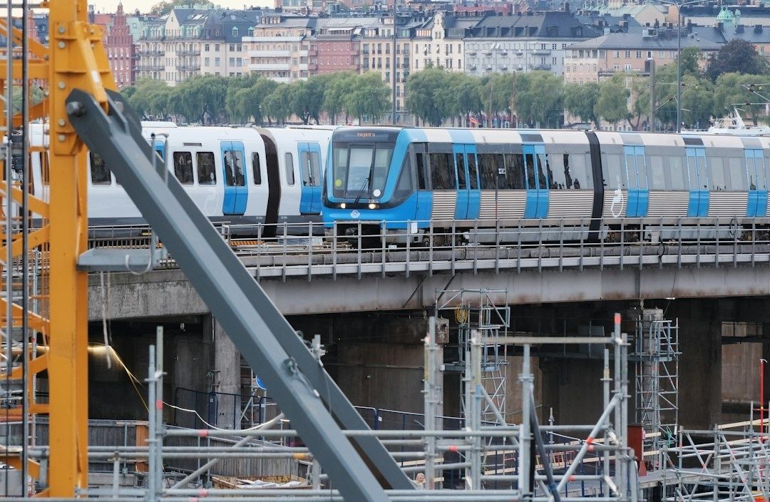 Blått pendeltåg på en bro, med stadsbebyggelse i bakgrunden