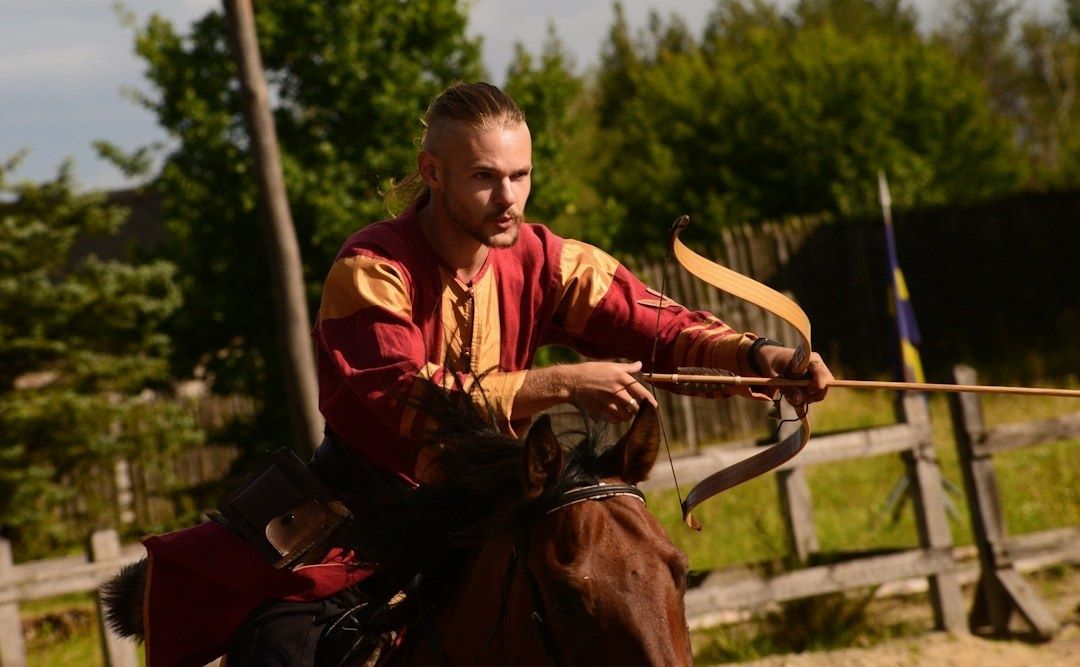 Medeltidsklädd bågskytt rider på en häst utomhus